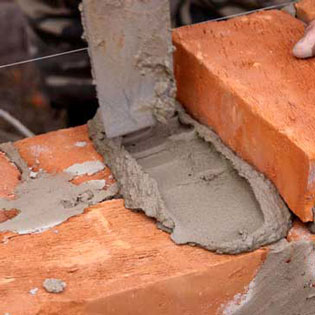 ouvrier en train de poser du ciment entre des briques